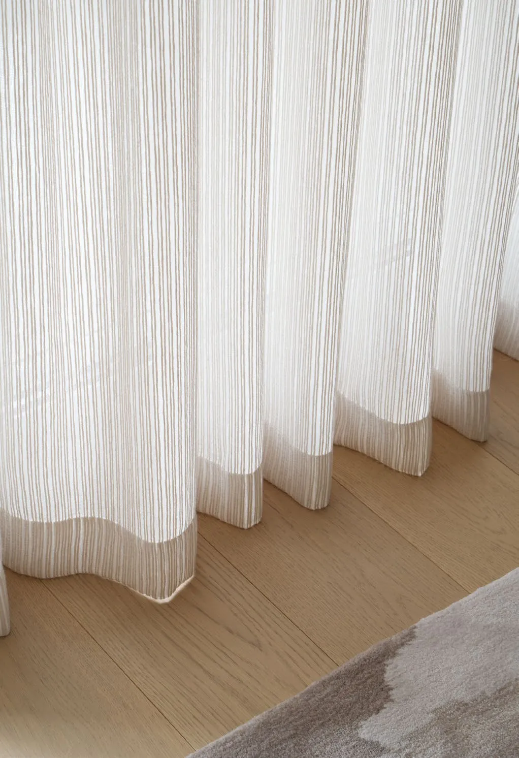 Striped sheer curtain pooling lightly over a pale oak floor