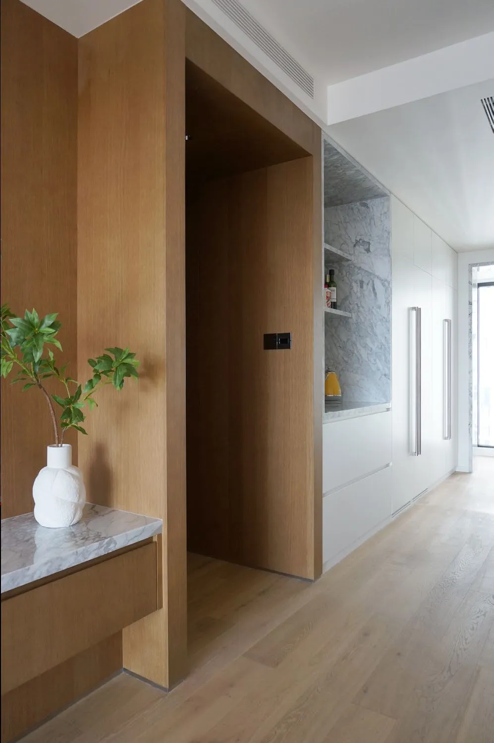 Great room of Y Residence with pale marble, white walls and warm wood cabinetry